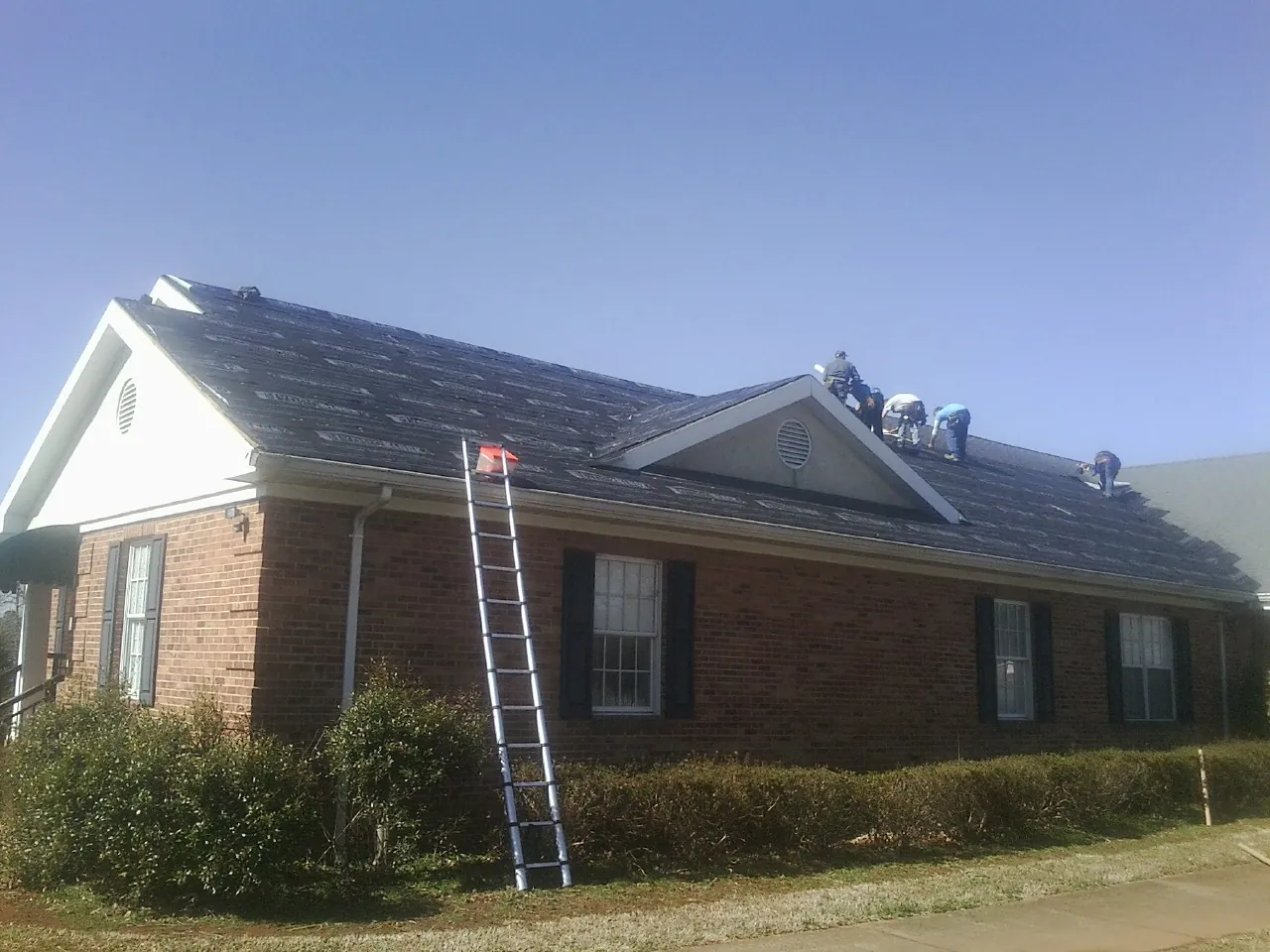 Crew tearing shingles off a brick ranch roof with a ladder set — Emergency Roof Repair work by our crew in Hudgins
