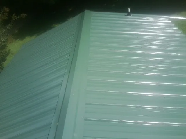 New green metal panels meeting at the ridge of a roof — Flat Roof Repair work by our crew in Hudgins