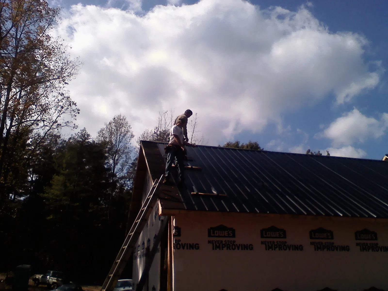 Roofer fastening dark metal panels high against a cloudy sky, from a Roof Inspection job in Hudgins