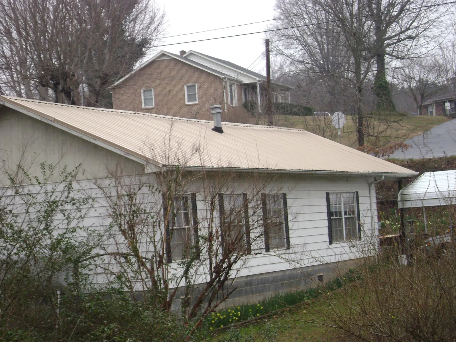 Tan metal roof on a white sided house set into a hillside — Commercial Roofing by Roofing Brothers in Hudgins